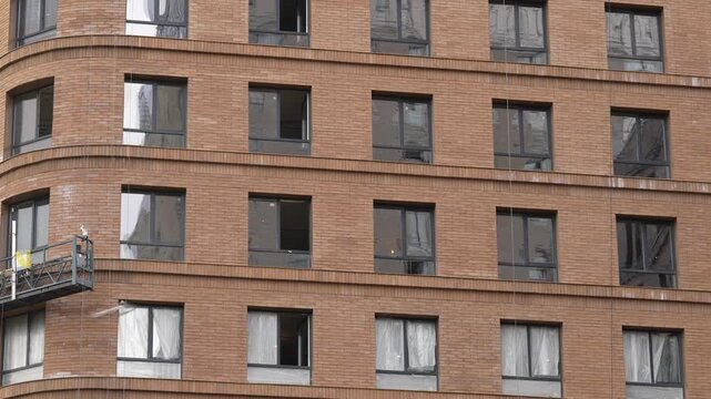 Residential building under construction with unfinished brick facade, installed windows and ongoing exterior works during urban development process
