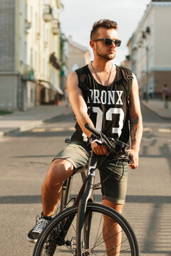 Young hipster man with bicycle sitting on a bicycle in the city. Black T-shirt with print 23