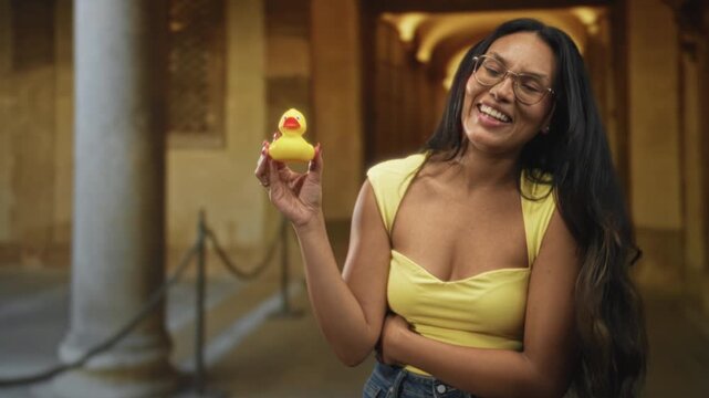 Woman holding yellow rubber duck while smiling and showing cleavage in ornate building corridor; playful joy.
