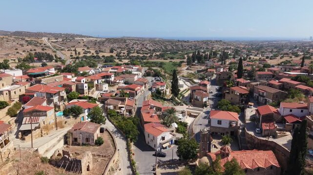 Panoramic view of Tochni village in Cyprus with traditional stone houses, red tiled roofs, cypress trees, rural roads and dry Mediterranean hills stretching toward the coast