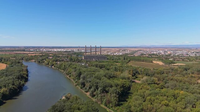 Hungary, decommissioned AES Tisza coal-fired power plant beside the Tisza River with smokestacks, fields and woodland in summer under clear sky, filmed by drone.