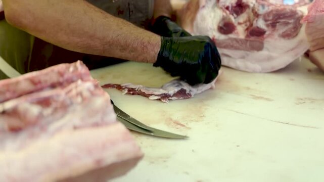 Professional butcher cutting raw meat with a sharp knife wearing black gloves in a commercial kitchen stock footage video clip.
