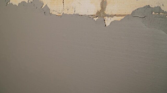 Video reveals an unfinished aerated concrete block wall behind a freshly applied layer of wet gray plaster. Close up shot showing construction, renovation, and home improvement process