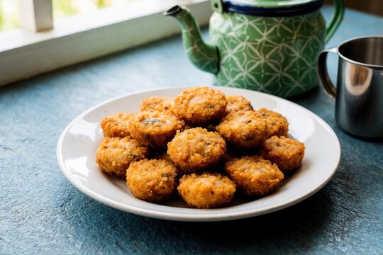Plate of otak otak fish cakes ready to eat. Indonesian seafood snack served hot. Savory bite sized appetisers, simple food preparation in rustic style with tea pot.