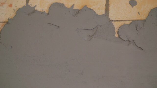 Video shows process of wall renovation. Close up of worker applying fresh grey cement mortar to aerated concrete block wall. Construction and repair work in progress