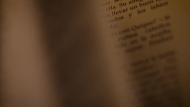 Close-up of a person turning pages of an old book in a cozy, intimate low-key room.