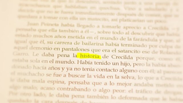 High-angle close-up of an open book in Spanish with the word 'historia' highlighted in yellow under dim lighting.
