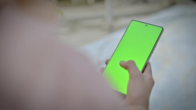 Woman holding smartphone with green screen mockup, female hands using mobile phone chroma key display for video replacement, close up interactive touch screen on light background
