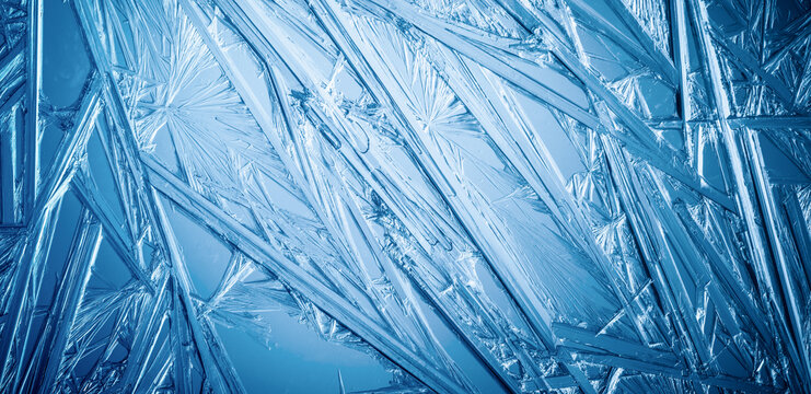 Ice frozen in intricate patterns of delicate crystals with brilliant contrasts of deep blues. Real unique patterned crystal formations. Sparkling window frost or icy cold winter frosting background.
