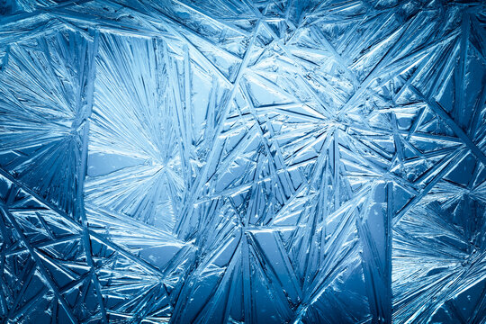Ice frozen in intricate patterns of delicate crystals with brilliant contrasts of deep blues. Real unique patterned crystal formations. Sparkling window frost or icy cold winter frosting background.
