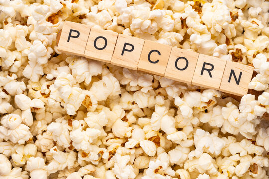 Scattered white popcorn, minimalist photograph with ample copy space &ndash; Wooden blocks spelling out "POPCORN".