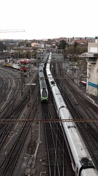 Bern, Switzerland - 20 May 2026: Bern Central Railway station. Overhead shot of railway tracks. Multiple trains travel parallel. City skyline in background. Close-up of silver train. Green front light