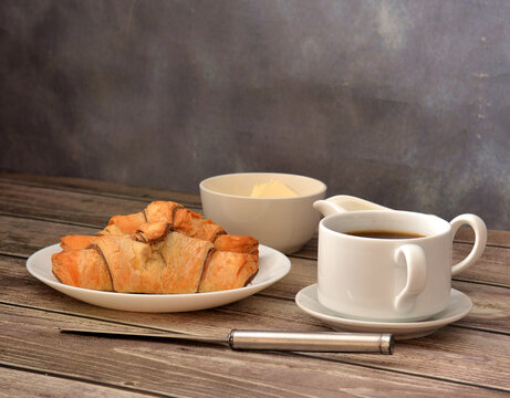 Light breakfast, black coffee, cream, two fresh croissants and butter on a wooden table.