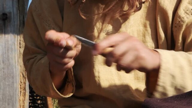 Reenactor craftsman in medieval costume whittling small wooden spoon using carving knife, historical craft
