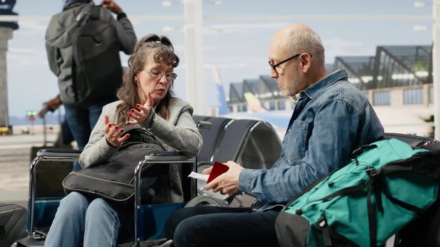 Older woman using a wheelchair and her husband check boarding pass information while waiting at the airport gate, highlighting mobility support, accessibility, equal opportunity and independence.