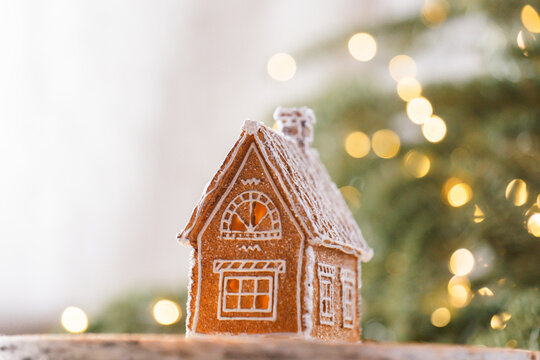 festive seasonal christmas Gingerbread house. Festive winter decor.Snow covered gingerbread house on a birch wood slice,Christmas setting with a glowing tree in the background.Christmas and New Year