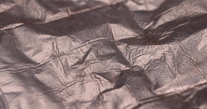 Water drops on crumpled metallic foil background texture, shiny aluminum wrap material with many clear liquid droplets on creased surface