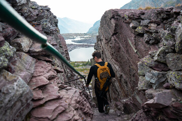 A hiker with a backpack walks down a steep rocky mountain path during an outdoor adventure. The natural setting creates an inspiring mood suitable for travel and fitness campaigns © Viks