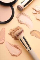 Swatches of different foundations, face powders and brushes on beige background, flat lay