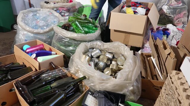 Volunteer sorting recyclables at recycling center, sustainable waste management. Waste, plastic, metal cans, cardboard, textiles, shoes, glass bottles and old electronics