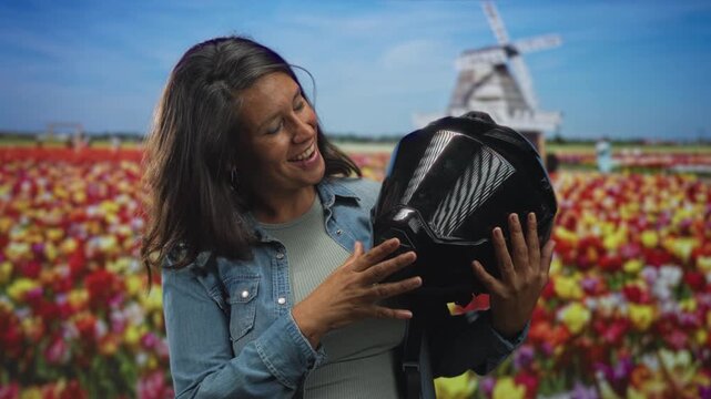 Woman holding black motorbike helmet and touching the visor with hand in studio; joyful travel anticipation.