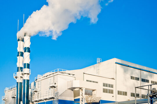 A heating plant and pipes emitting white smoke, with a pipeline in the foreground and a blue sky in the background