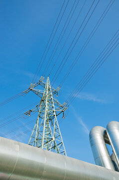 The photo shows a pipeline and a power transmission tower against a blue sky