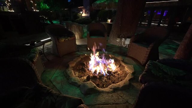 Gas fire pit burning at night surrounded by wicker patio chairs