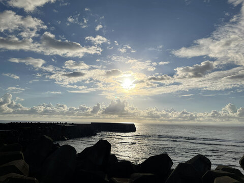 Bright sunlight breaking through dramatic clouds over the sea with a silhouette of breakwaters in Okinoerabu Island, Kagoshima, Japan.