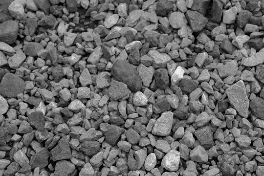 大小様々な灰色の石や砂利が地面を一面に覆っている、建設現場や庭園の基礎となる素材を示すモノクロのクローズアップ写真。粗い質感と不規則な形状が特徴的。