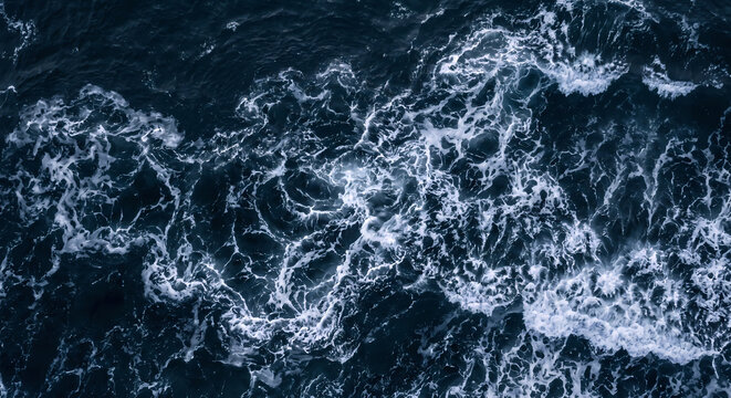 A turbulent dark blue ocean surface churns with rolling sea foam and powerful tidal currents that create complex liquid patterns beneath the vast movement of shifting maritime saltwater waves