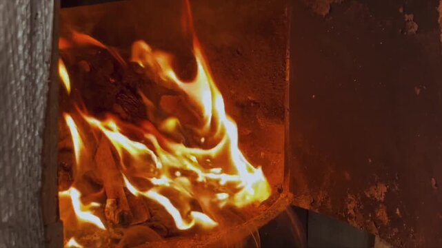 Bright orange flames and burning firewood inside a metal furnace firebox close-up