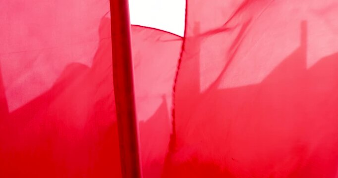 Red flags waving in the wind against a cloudy sky, several bright fabric flags on flagpoles flutter during an outdoor holiday celebration, no person
