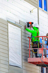 Construction worker installing siding planks with pneumatic nail gun from boom lift in USA © Andrei Liashchou