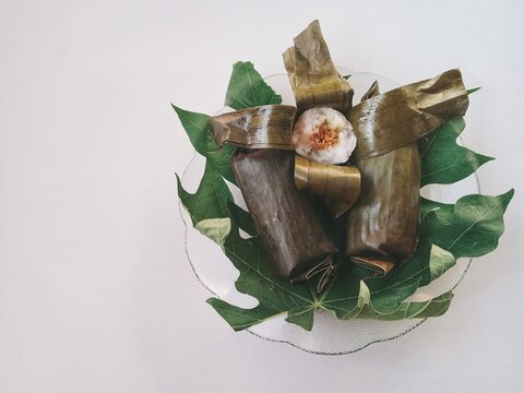 Three wrapped rice dumplings rest on green leaves, and Close-up photo at a 45-degree angle.