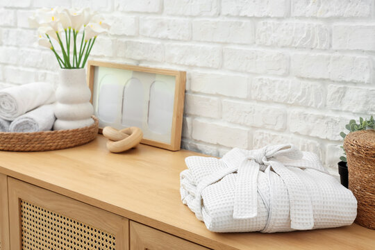 Folded bathrobe on commode near white brick wall in bathroom