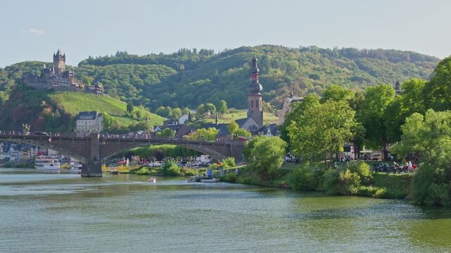 Scenic panoramic cinematic landscape video of Cochem town, the historic stone bridge crossing the Moselle river, lush green hills with vineyards, and the majestic Reichsburg Cochem castle in Rhineland