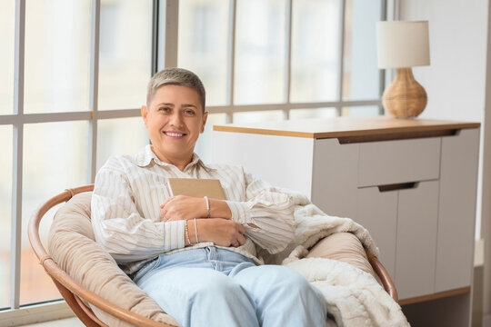 Young woman with short hair and book sitting in armchair at home