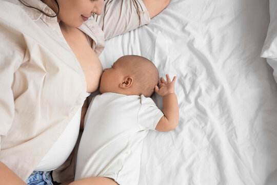 Young mother breastfeeding her baby on bed, top view