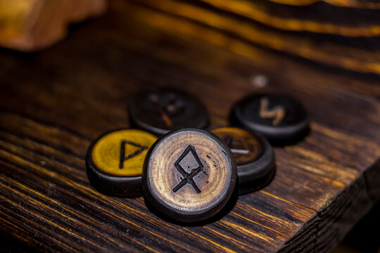 Handcrafted wooden runes with engraved ancient symbols resting on a weathered rustic timber surface, capturing a mystical atmosphere and esoteric Nordic folklore tradition, Odal rune in the center