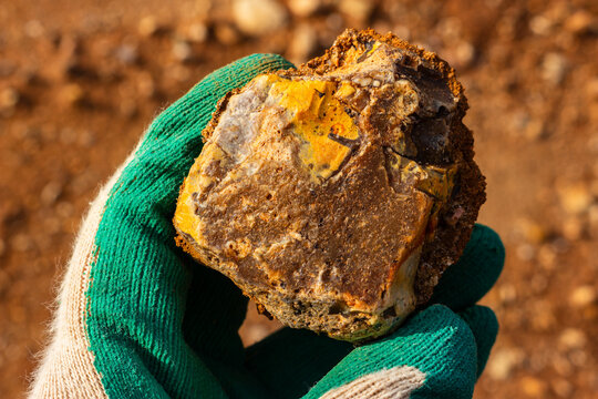 Close-up view of a hand in a green work glove holding a piece of raw flint stone found at a quarry site with textured mineral surface and earthy tones