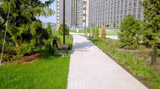Modern residential complex with walking path, wooden benches, and green landscaping in a summer city park