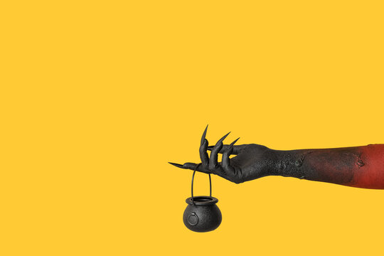Black hand of witch with cauldron on yellow background. Halloween celebration