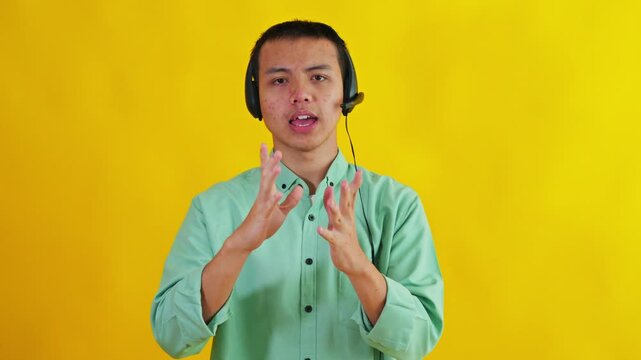 Asian customer service agent wearing headset talking and explaining with hand gestures on yellow backdrop