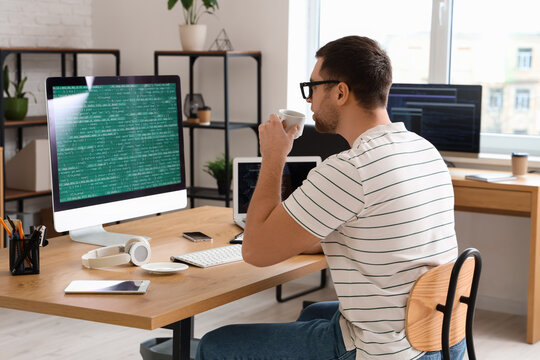 Portrait of male programmer drinking coffee at his workspace in office