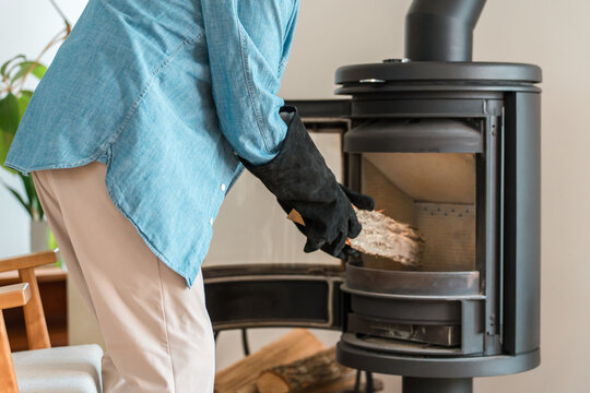 Senior Man Adding Firewood to a Wood-Burning Stove to Keep Warm, Winter Living in a Cozy Home