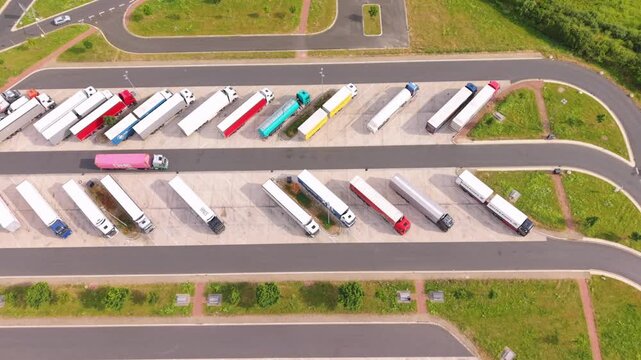 Aerial perspective of a logistics yard filled with parked trucks of different colors and sizes, surrounded by green grass and roadways