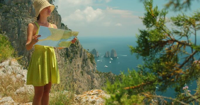 Traveler woman exploring Capri cliffs with map under summer sky above Tyrrhenian Sea during hiking tour
