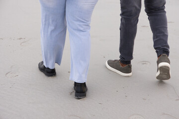 Obraz premium Couple walking on sand leaving footprints, wearing light blue pants and black boots, gray sneakers