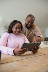 Obraz premium African couple sitting at wood table with tablet case, man pointing, in pink sweater beige pullover